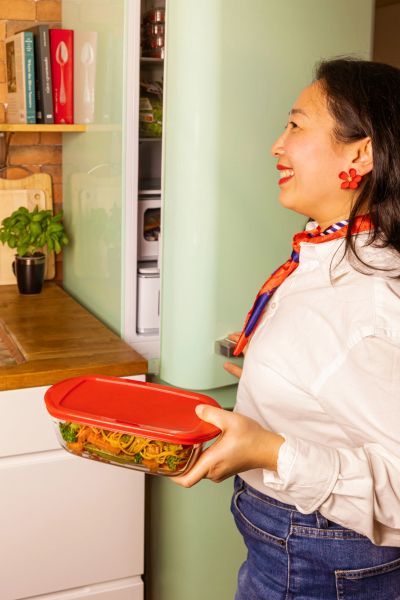 Жена поставя стъклена кутия oCuisine с капак в хладилник – безопасна за съхранение и повторно затопляне на храна, с практичен червен капак